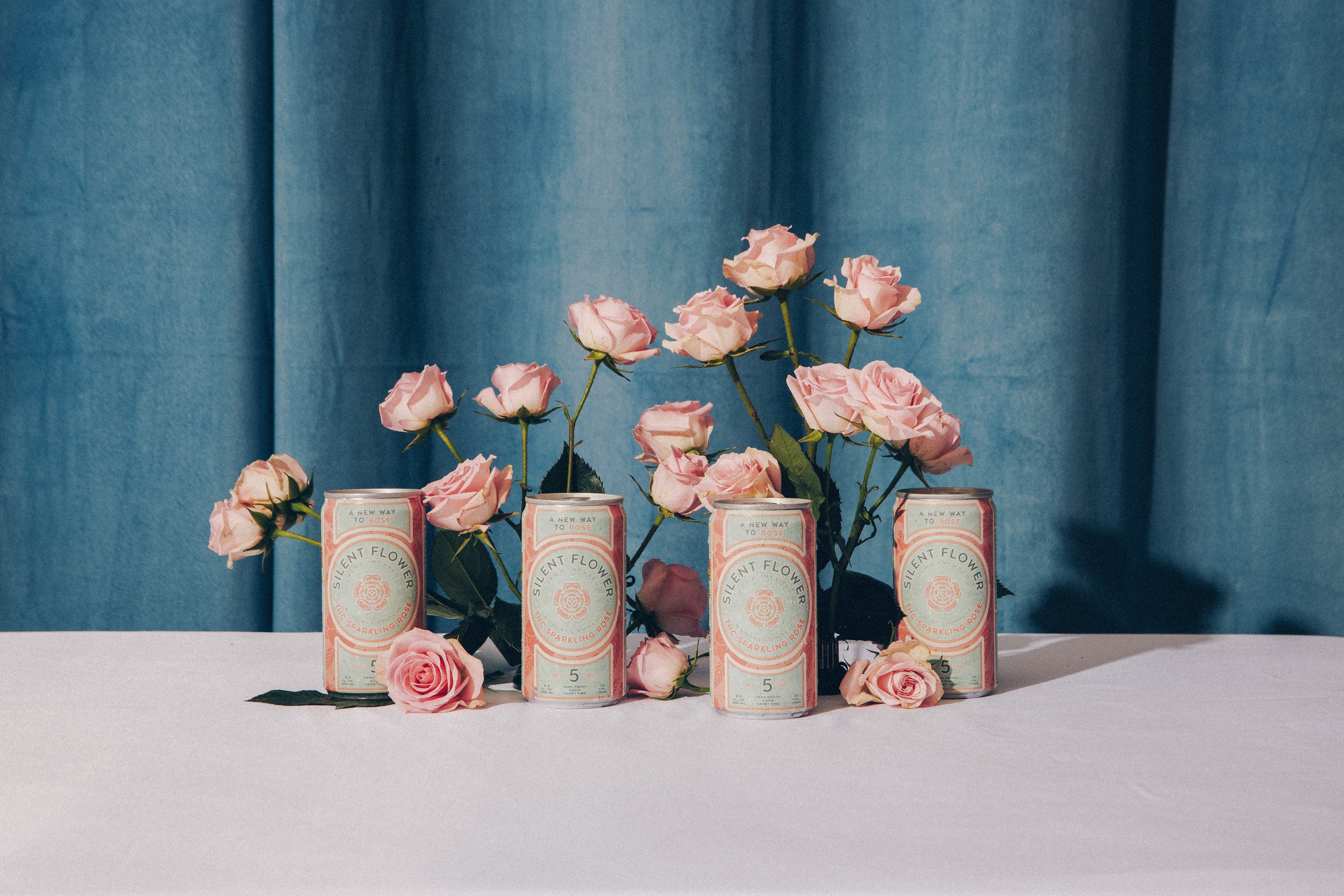 Four cylindrical cans with decorative labels and pink flowers on a blue curtain background